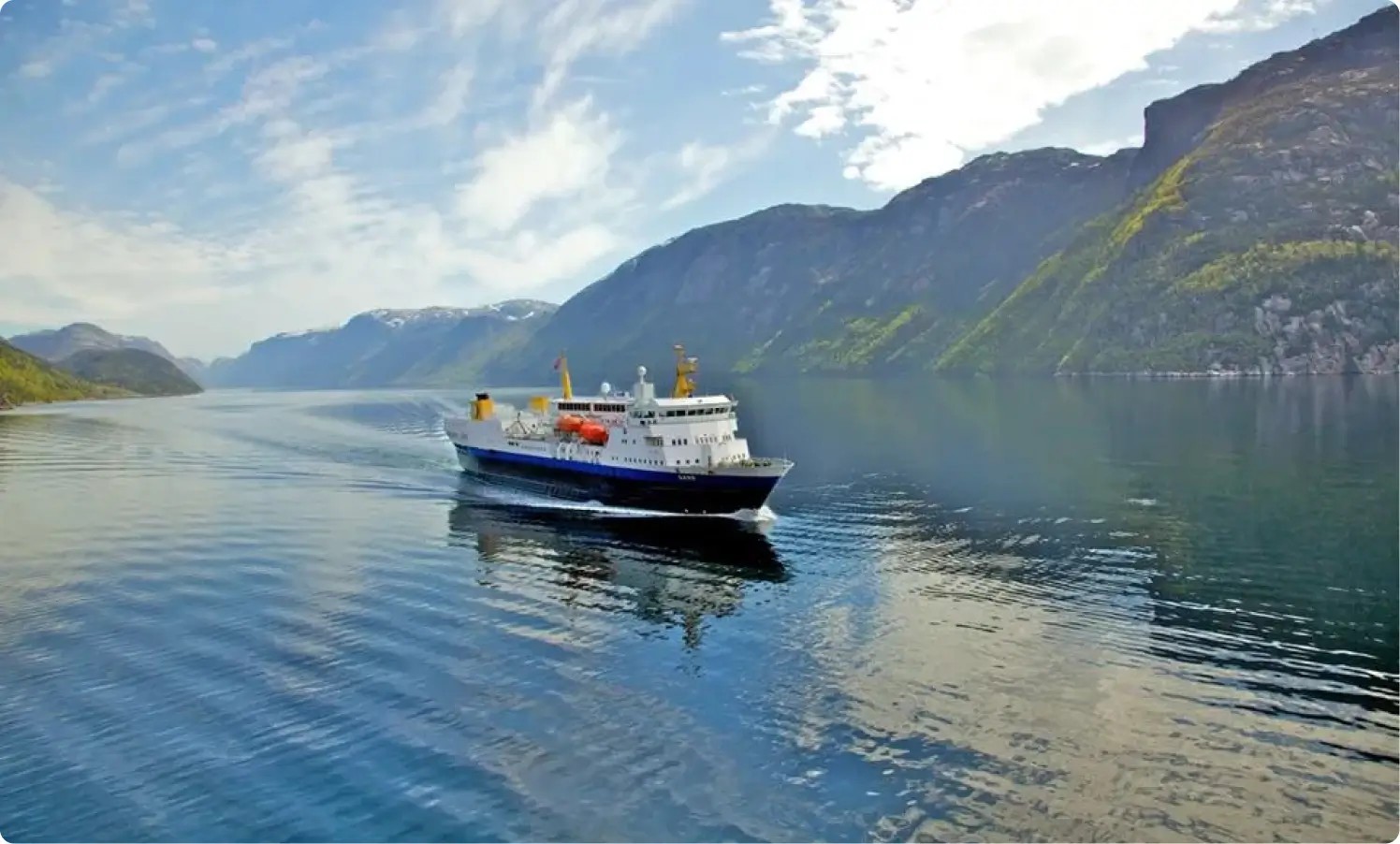 Båt seiler inn i en fjord omgitt av fjell